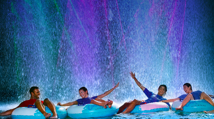 Visitors on lazy river with vivid LED lighting on water curtain at night